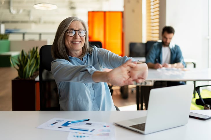 Happy senior woman eager to work cracking her knuckles and flexing her fingers while sitting at her laptop in the office