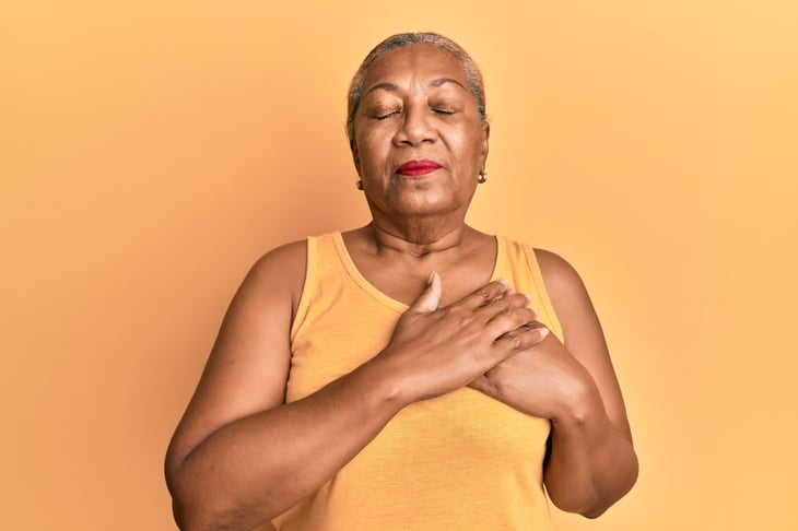 Senior woman with eyes closed and hands to her heart.