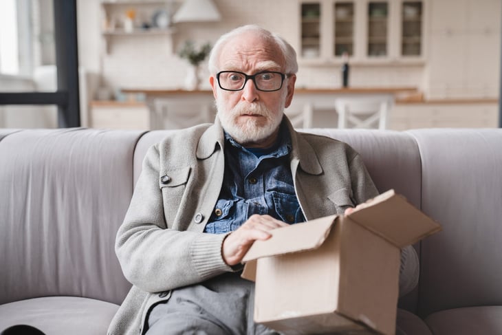 Shocked and disappointed senior man opening a package he wants to return