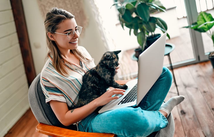 A woman holds her cat while using a laptop