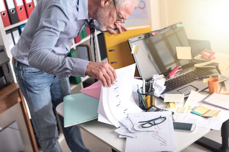 older man looking through cluttered desk
