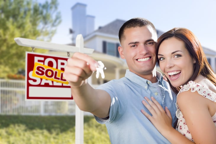 Couple in front of a home with a "sold" sign.