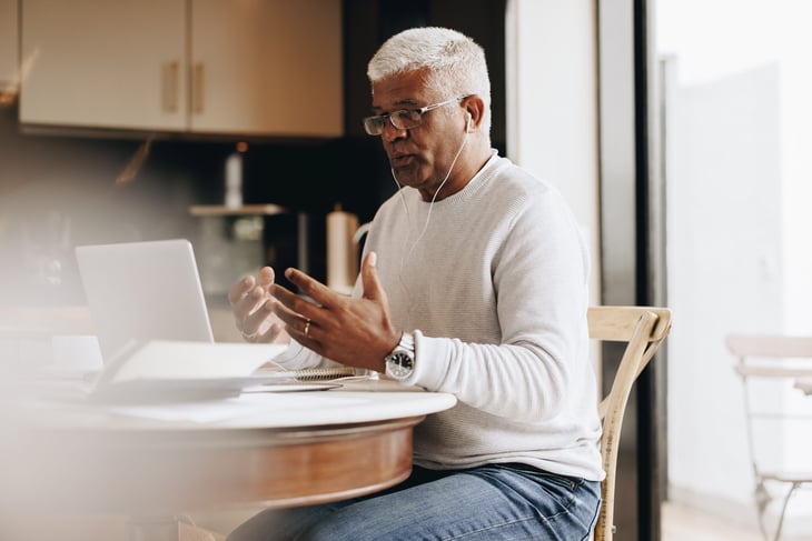 Senior worker working remotely on laptop in kitchen or home office