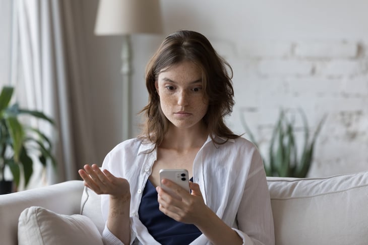 Frustrated or confused woman at home looking at her phone in frustration and annoyance