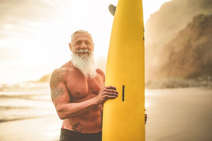 A fit senior holding a surfboard at the beach