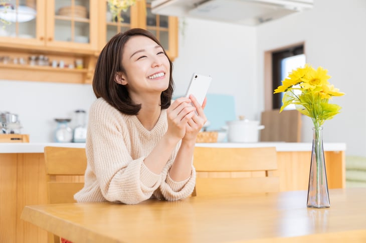 Happy woman using smartphone in the kitchen and thinking