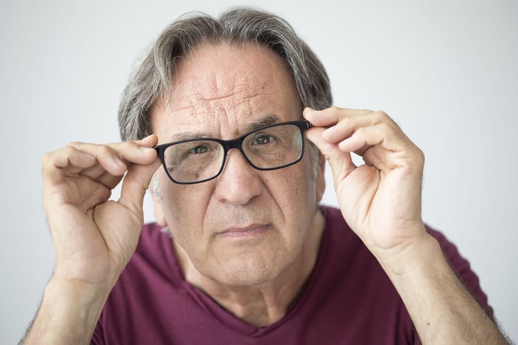 Senior looking carefully through his glasses squinting and surprised