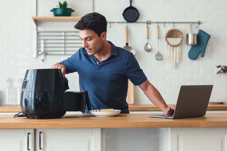 Man in the kitchen using an air fryer and his laptop for recipes to cook a meal
