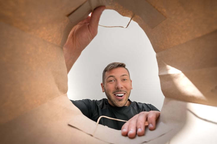 Excited, happy, smiling man looking inside a paper bag from the grocery store