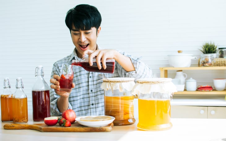 Man smiling while pouring some of his homemade kombucha.