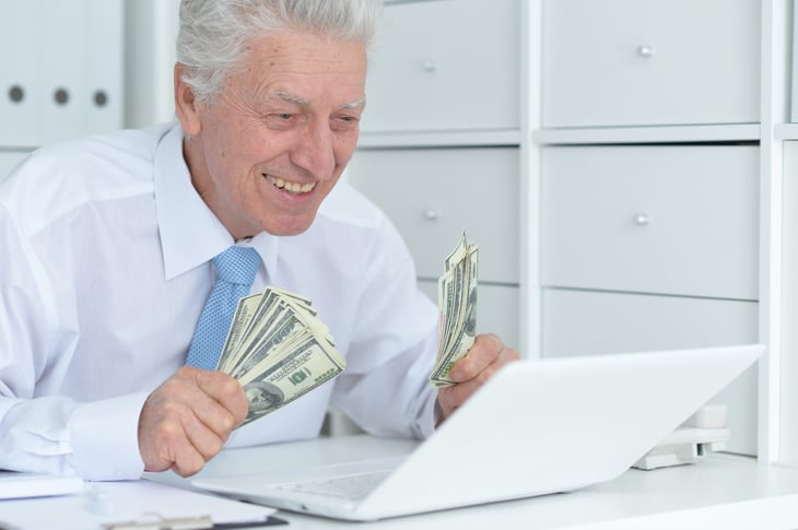 senior man holding cash looking at computer