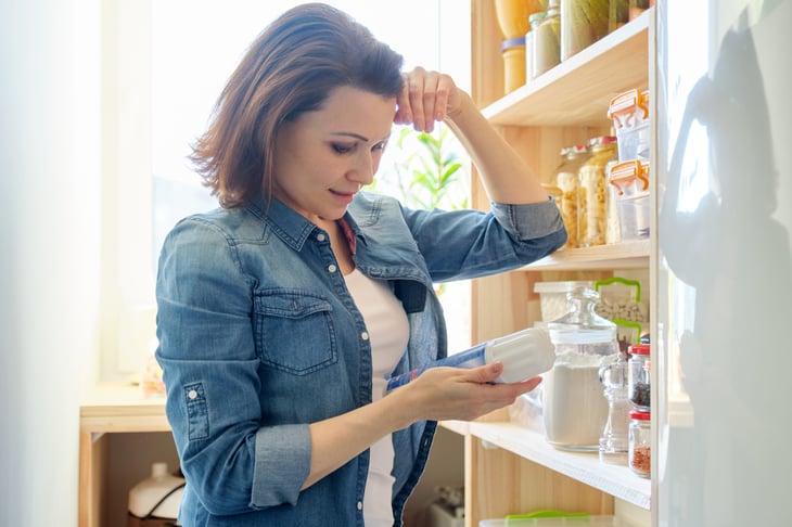Woman looking thoughtful or confused in pantry examining container