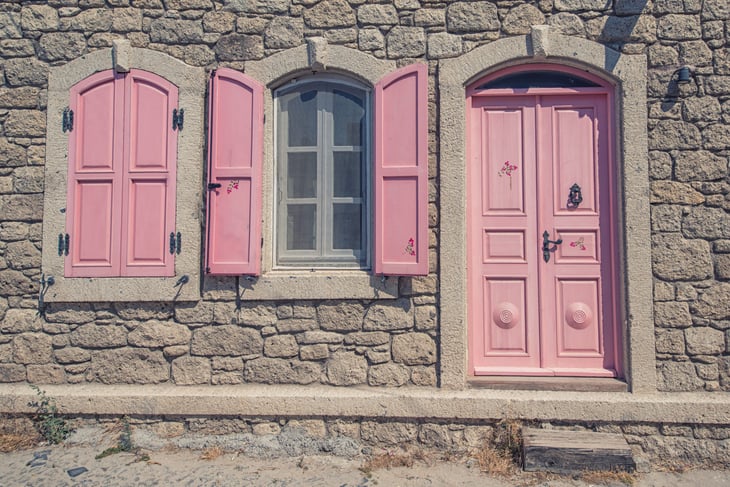 A stone house with a pale pink front door and shutters.