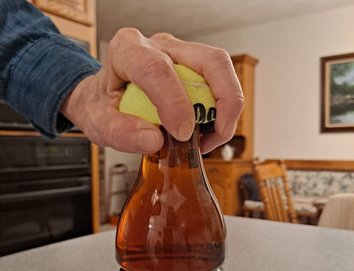 Tennis ball used as a bottle opener aid