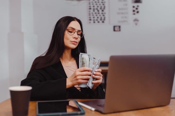 Woman counting extra money at laptop