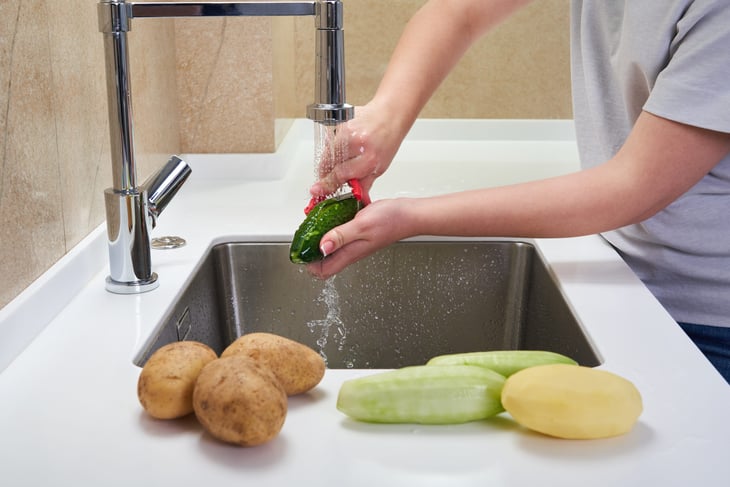 Man cutting vegetables in kitchen sink and using garbage disposal