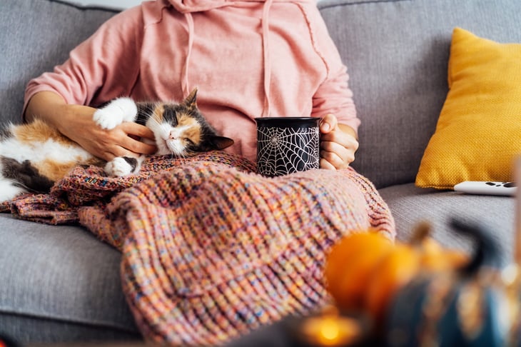 Woman watching TV in autumn with a cat and spooky coffee mug in her lap