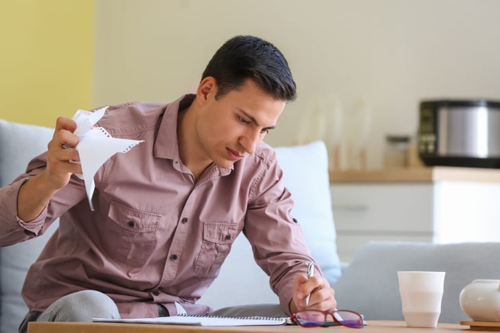 Man crumpling paper in frustration and stress, writing in a notebook, planning or doing math or taking notes