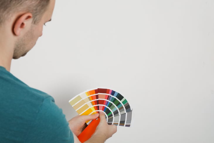 Man with palette choosing color for painting wall indoors. Interior design.