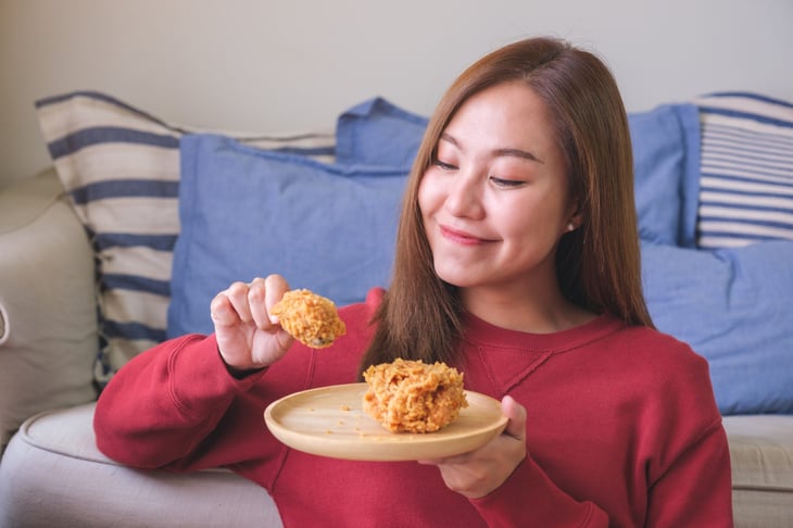 Smiling woman eating fried chicken at home