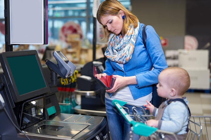 Young mother paying at grocery checkout with baby in cart