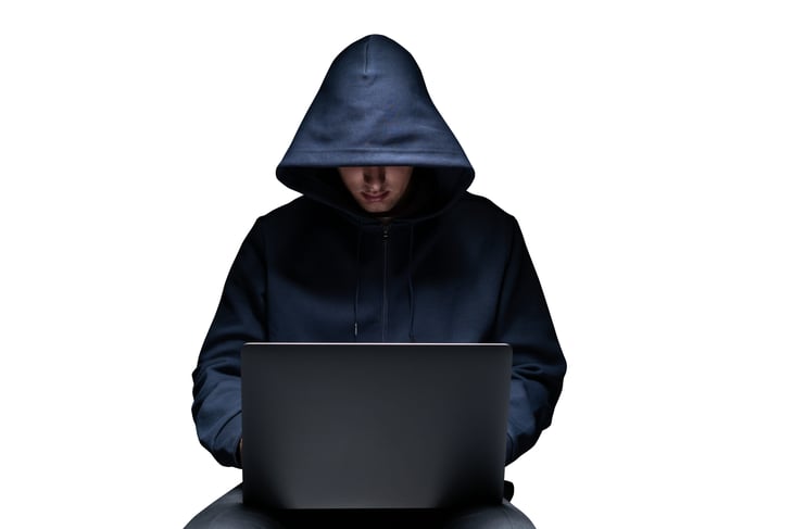An unrecognizable young hacker in black hoodie using laptop.