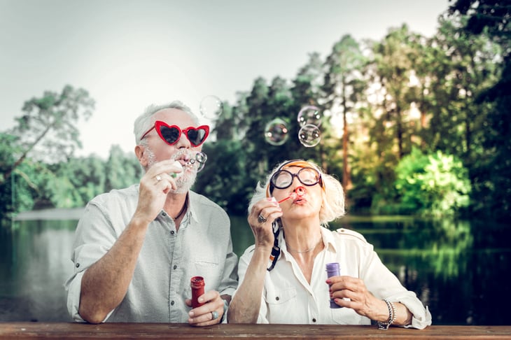 Senior couple sit at a picnic table and blow bubbles