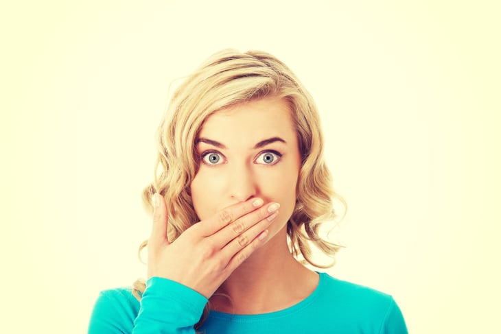Woman shocked or embarrassed and making an "oops" face covering her mouth after making a mistake