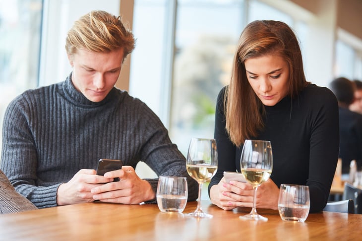 Rude couple using phones at the dinner table in a restaurant ignoring conversation