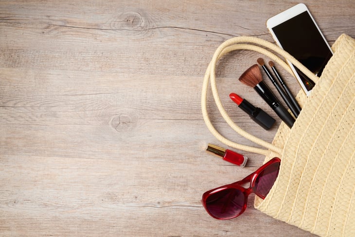 Table covered in personal belongings like sunglasses, phone, makeup and bag