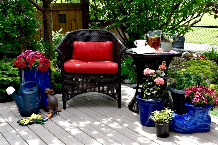 Shaded patio with flowers, green plants, and a table and chair