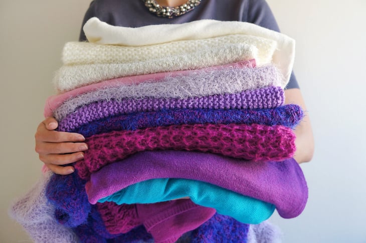 Woman holding a pile of sweaters and colorful laundry