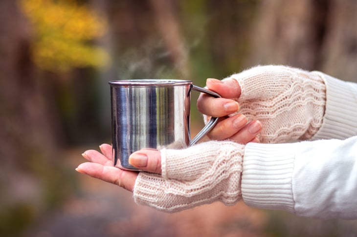 Woman with fingerless gloves on her hands holding a cup of hot chocolate or some warm winter drink