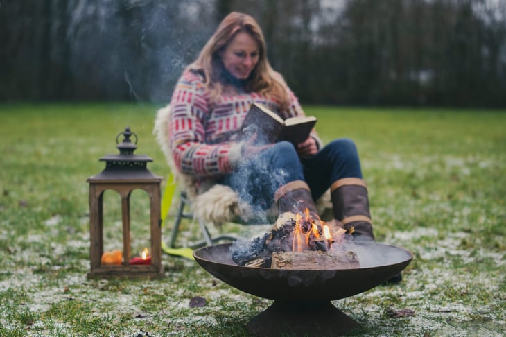 woman outside reading by winter campfire