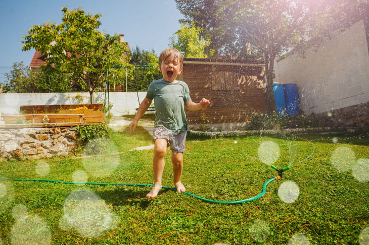 Child yelling and playing in a sprinkler