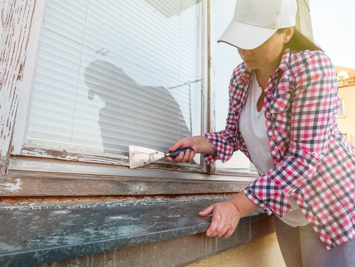 Woman scraping paint off the outside of a window