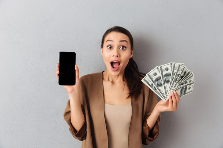 Excited woman holding cash and her phone