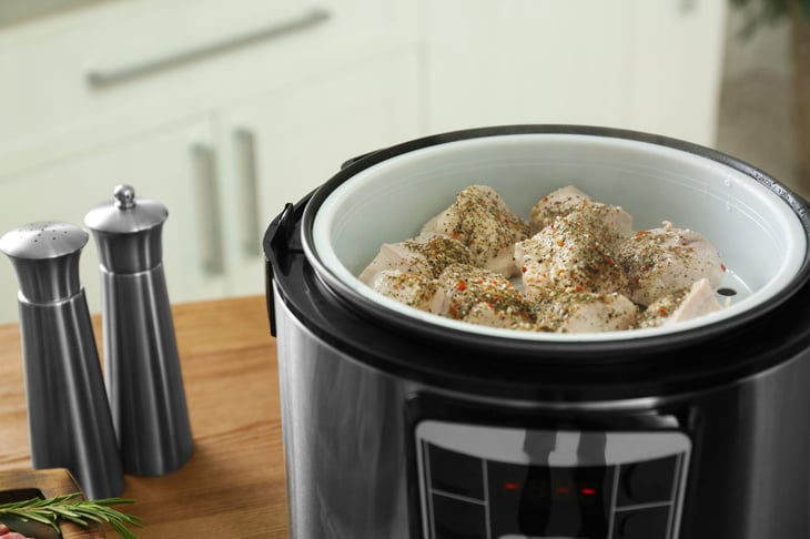 chicken with spices in slow cooker on wooden table
