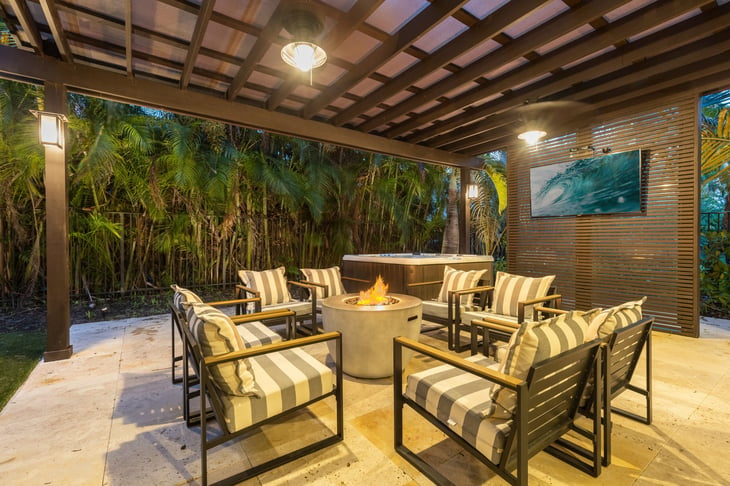 Covered lanai with Jacuzzi, round fire pit with lounge chairs, wall of palm trees, ceiling fans and TV