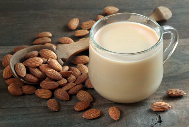 Almond milk in a glass cup and almonds on a table.