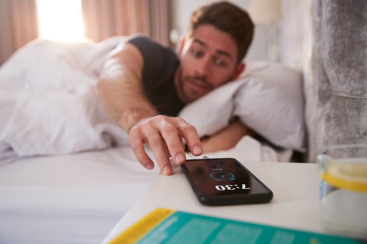 Man in bed turning off phone alarm in the morning