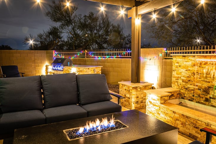 A backyard at night with a waterfall, pergola, and a firepit at night.