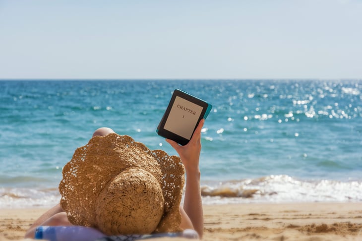Woman reading a book on an e-reader on the beach
