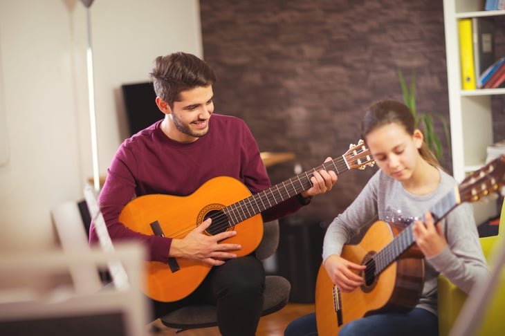 Man teaching girl to play guitar, father and daughter playing music together