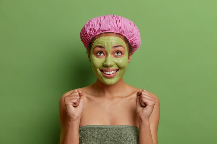 woman in bath hat and towel applies nourishing avocado mask