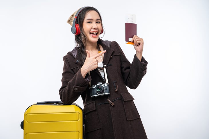 Happy woman wearing headphones and holding passport ready to travel with her luggage suitacase