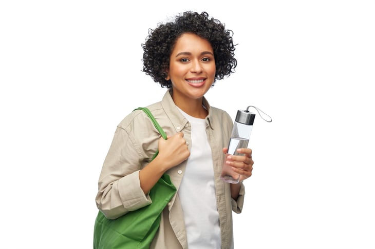 smiling woman with water in reusable glass bottle and shopping bag