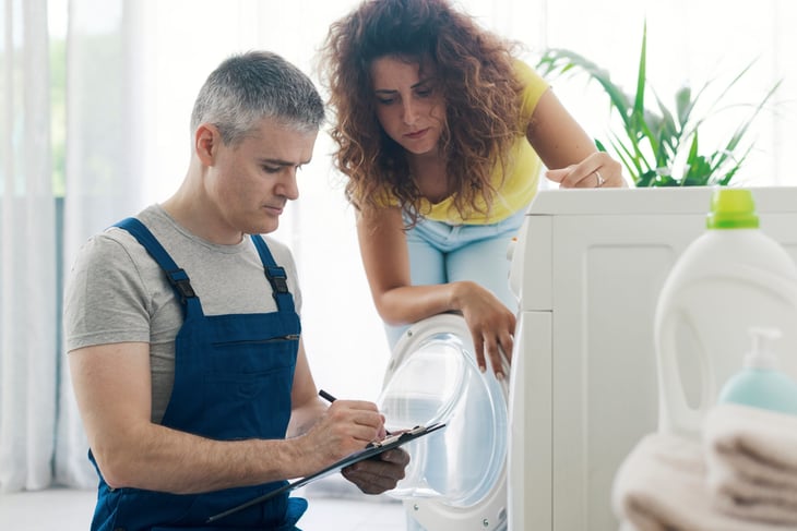 Technician writing up an invoice for a woman's washing machine repairs.