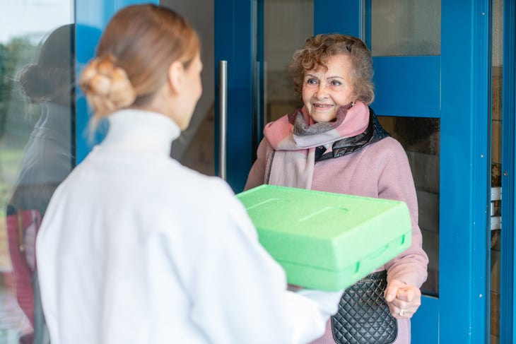 Woman delivering a hot meal to a smiling senior woman through a program such as Meals on Wheels