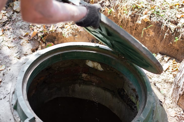 The man opens a sewer hatch. Septic tank inspection and maintenance.
